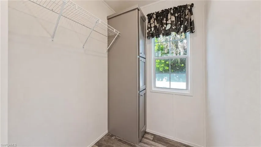 Wardrobe area featuring wire shelving, built-in cabinetry, wood-finish flooring, and a window with white trim