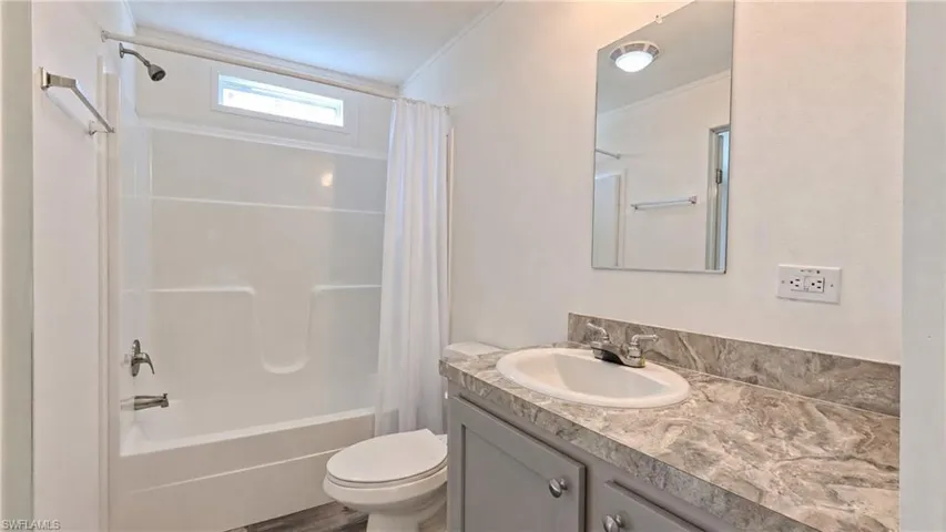 Full bathroom featuring a white tub/shower combination with an upper window, a toilet, and a vanity with a countertop and under-sink cabinetry