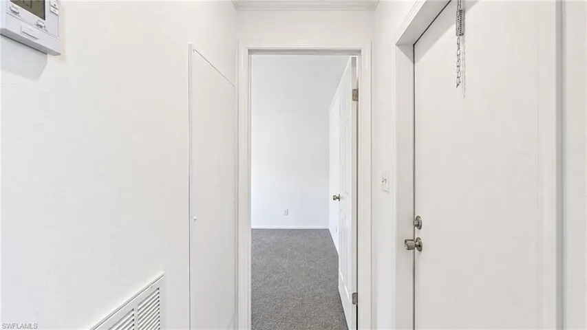 Interior hallway featuring white painted walls and trim, a white door with brushed nickel hardware, and a digital thermostat