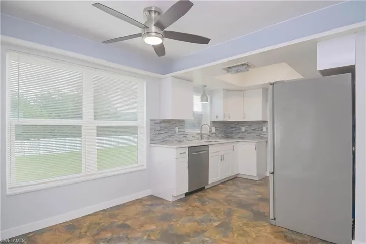 Kitchen with stainless steel dishwasher, sink, ceiling fan, white refrigerator, and white cabinets