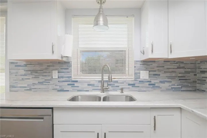 Kitchen with hanging light fixtures, sink, light stone countertops, and decorative backsplash