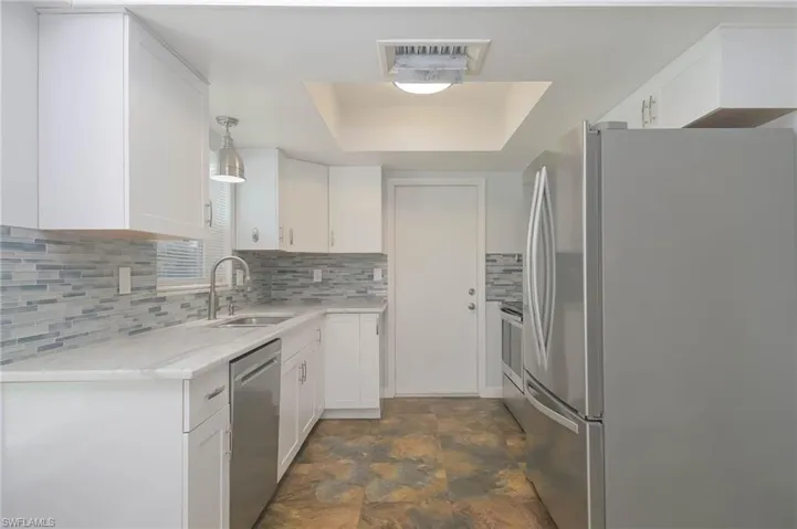 Kitchen with decorative light fixtures, backsplash, appliances with stainless steel finishes, sink, and white cabinets