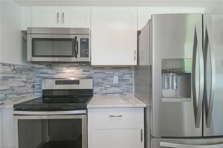 Kitchen with light stone countertops, stainless steel appliances, white cabinetry, and backsplash