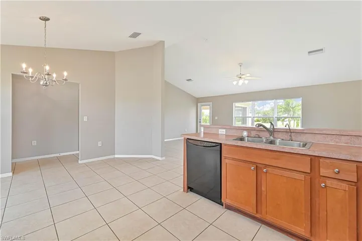 Kitchen featuring lofted ceiling, a chandelier, black dishwasher, light countertops, and brown cabinetry