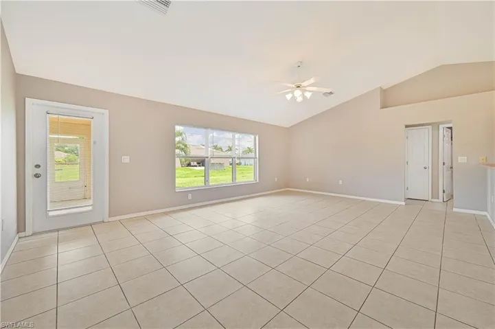 Empty room with lofted ceiling, ceiling fan, light tile patterned flooring, and plenty of natural light