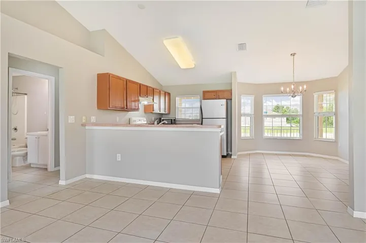 Kitchen featuring light tile patterned flooring, a peninsula, a chandelier, brown cabinetry, and high vaulted ceiling