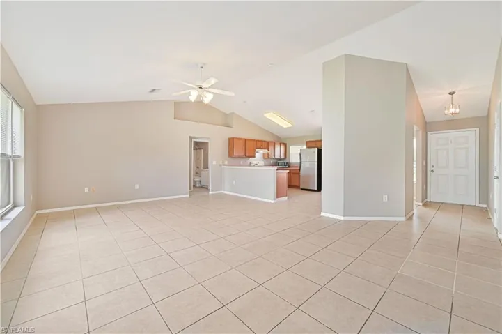 Unfurnished living room featuring light tile patterned floors, vaulted ceiling, healthy amount of natural light, and a ceiling fan