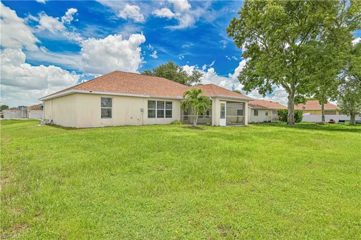 Rear view of property with a yard, stucco siding, and roof with shingles