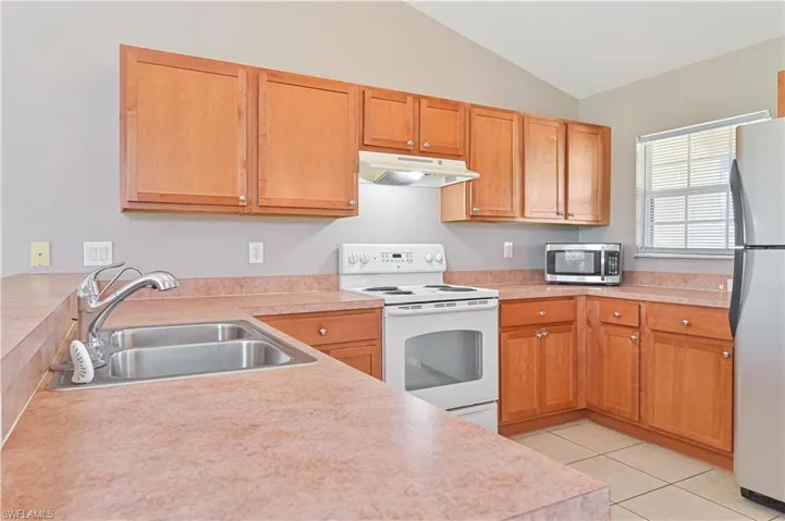 Kitchen with appliances with stainless steel finishes, vaulted ceiling, under cabinet range hood, light countertops, and light tile patterned floors