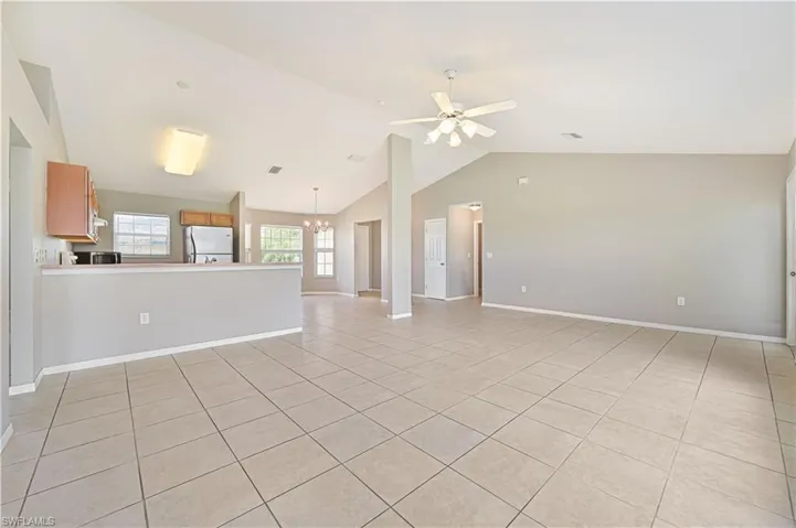 Unfurnished living room with light tile patterned floors, a chandelier, a ceiling fan, and lofted ceiling
