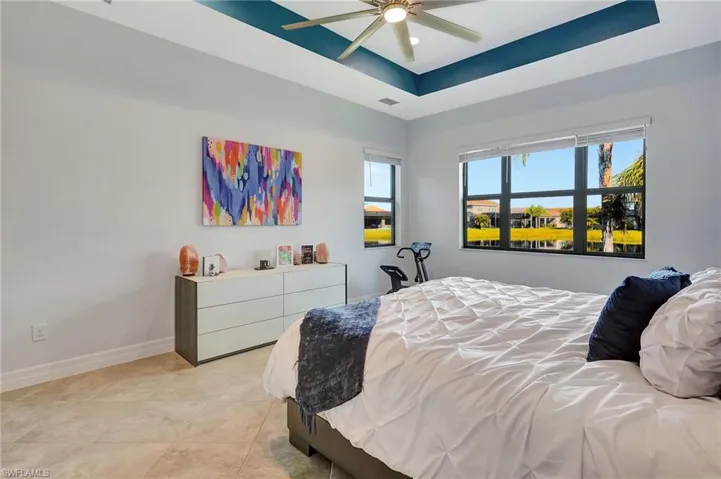 Bedroom featuring a raised ceiling, light tile patterned floors, and a ceiling fan