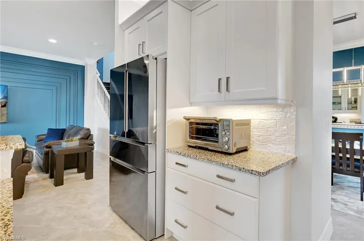 Kitchen with freestanding refrigerator, light stone countertops, white cabinetry, ornamental molding, and decorative backsplash