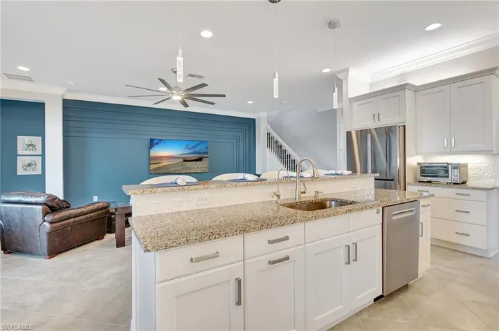 Kitchen with crown molding, appliances with stainless steel finishes, open floor plan, ceiling fan, and light stone countertops