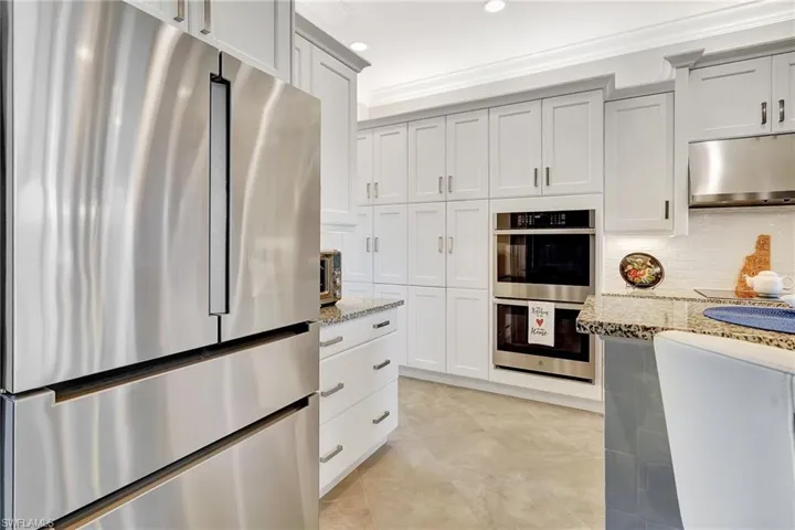 Kitchen featuring appliances with stainless steel finishes, ventilation hood, light stone countertops, ornamental molding, and decorative backsplash