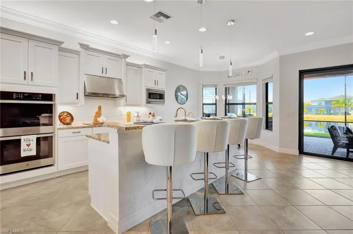 Kitchen featuring stainless steel appliances, under cabinet range hood, an island with sink, light tile patterned floors, and a breakfast bar