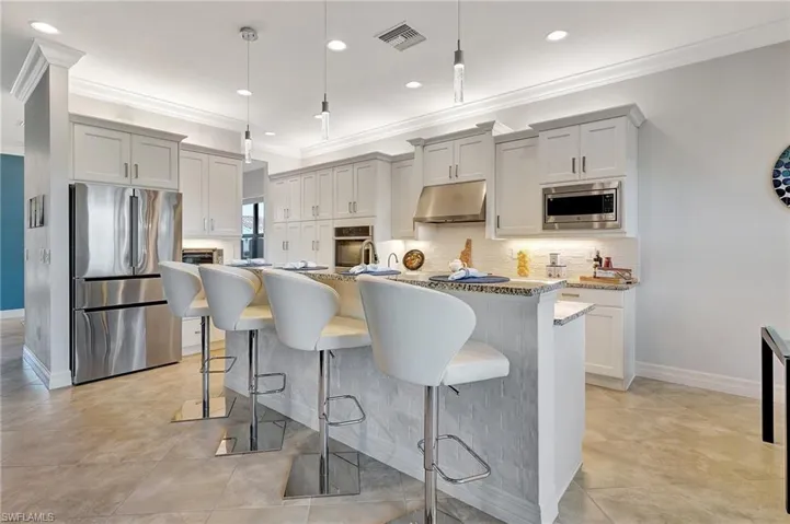 Kitchen with stainless steel appliances, under cabinet range hood, crown molding, a kitchen island with sink, and tasteful backsplash