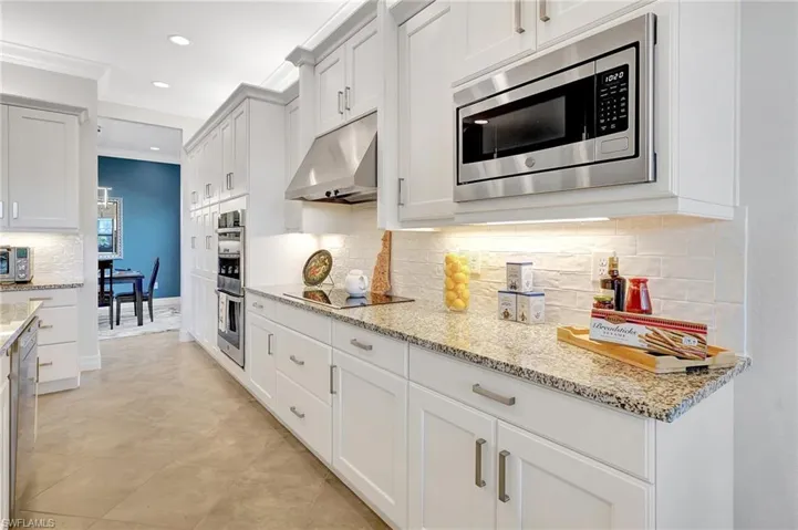 Kitchen featuring under cabinet range hood, appliances with stainless steel finishes, crown molding, recessed lighting, and light stone countertops