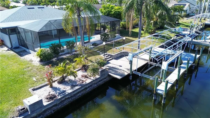 Dock area featuring boat lift, glass enclosure, a water view, a patio, and an outdoor pool