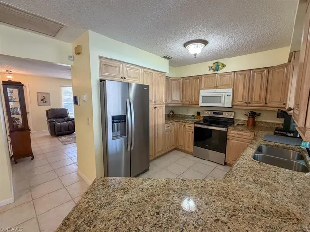 Kitchen featuring stainless steel appliances, light tile patterned floors, light stone countertops, and a textured ceiling