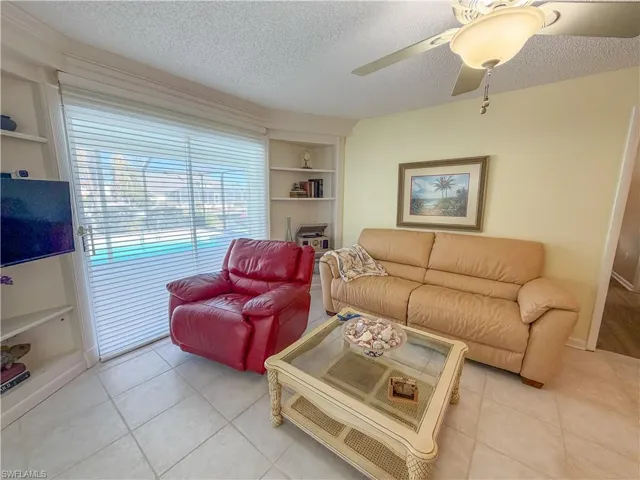 Living area featuring built in features, a textured ceiling, a ceiling fan, and light tile patterned floors