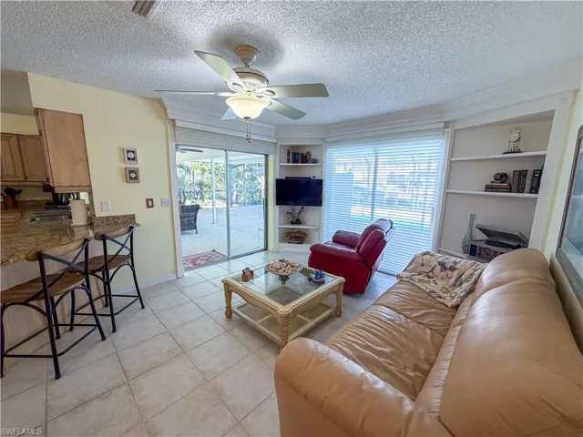 Living room with built in shelves, a textured ceiling, light tile patterned flooring, and a ceiling fan