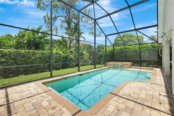 Screened-in pool deck featuring a swimming pool, integrated spa, and paver surfacing
