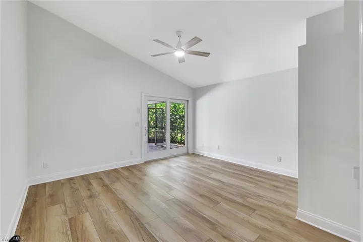 Vaulted ceiling, wood-finish flooring, ceiling fan, and white sliding glass doors