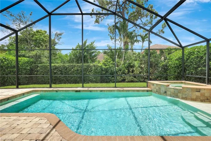 Screened-in outdoor pool featuring a hot tub with a stone-finish facade, integrated waterfall, and paved deck surround