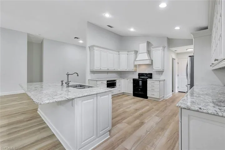 Kitchen featuring light wood-finish flooring, white cabinetry, a built-in oven, and a large central island with an integrated sink and light-toned countertop