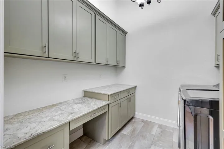 Cabinetry with light gray finish, granite-style countertops, integrated desk area, and tile flooring