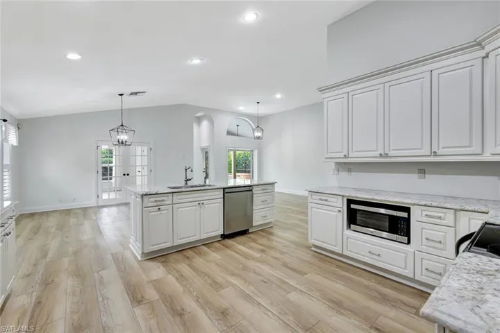 Open-concept living space with vaulted ceilings, wood-finish flooring, and white cabinetry