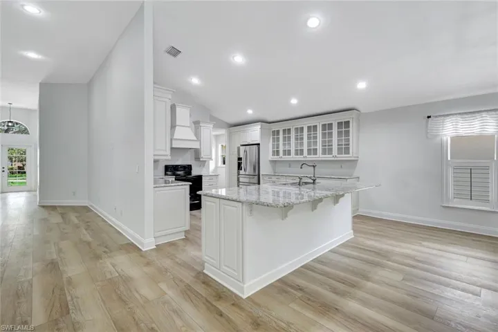 Spacious kitchen with a central island, white cabinetry, integrated range hood, and wood-finish flooring