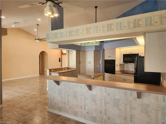 Kitchen featuring arched walkways, ceiling fan, a peninsula, black appliances, and vaulted ceiling