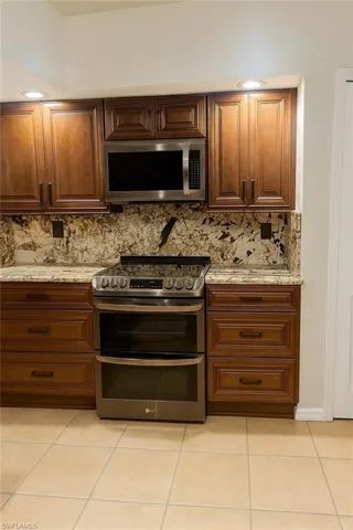 Kitchen with light tile patterned floors, stainless steel appliances, light stone countertops, and tasteful backsplash