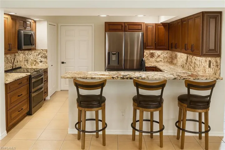 Kitchen featuring backsplash, appliances with stainless steel finishes, light tile patterned floors, a peninsula, and brown cabinetry
