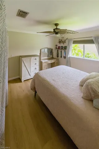 Guest bedroom 1 with wood finished floors, a ceiling fan, and ornamental molding