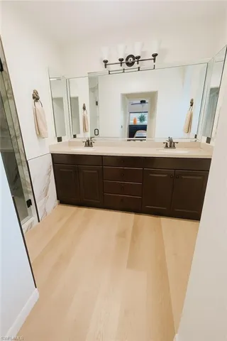 Bathroom with double vanity, light wood-type flooring, and a shower stall
