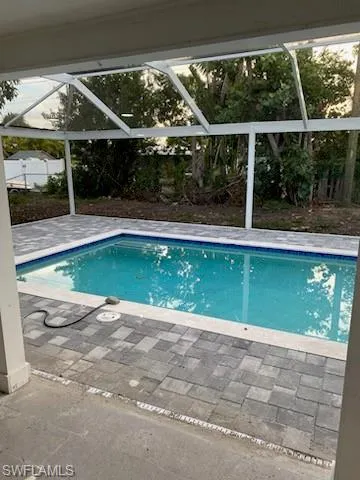 Screen-enclosed swimming pool featuring a cool-toned water, blue tile waterline, and surrounding paver deck