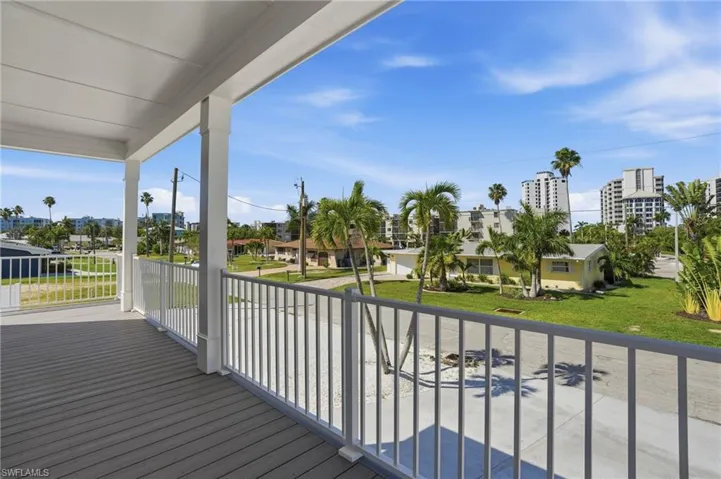 Elevated balcony with wood-finish flooring, white railing, and decorative columns - Virtually Edited Image