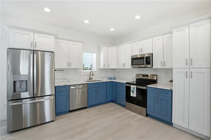 Contemporary kitchen featuring two-tone cabinetry, stainless steel appliances, marble-look countertops, a geometric tile backsplash, and light wood-finish flooring - Virtually Edited Image