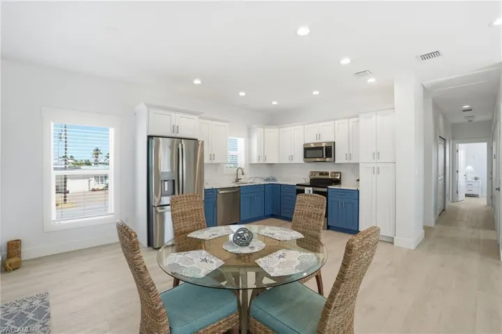 Open-concept kitchen and dining area featuring two-tone cabinetry, stainless steel appliances, recessed lighting, and wood-finish flooring - Virtually Edited Image