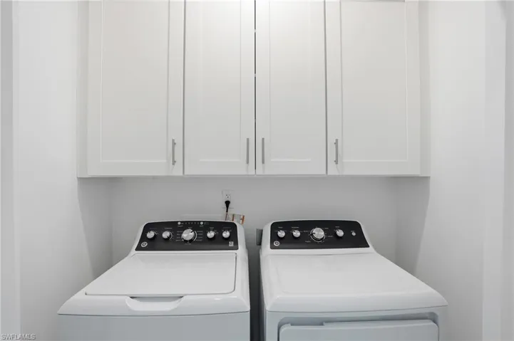 Dedicated laundry space featuring upper white cabinetry with brushed nickel hardware - Virtually Edited Image
