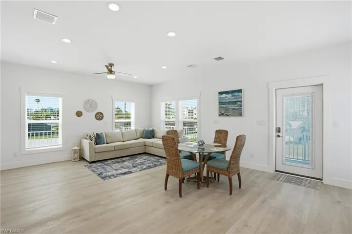 Expansive living area featuring light wood-finish flooring, white walls, and recessed lighting - Virtually Edited Image