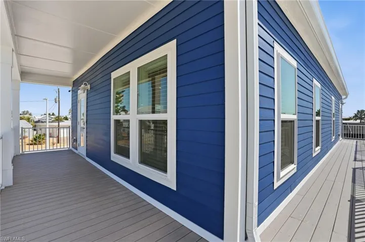 Exterior featuring blue horizontal siding, multiple windows with white trim, a covered porch with white columns, and gray decking - Virtually Edited Image