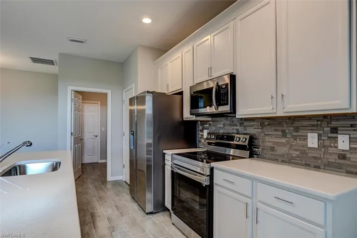 Kitchen with white cabinets, backsplash, stainless steel appliances, light hardwood / wood-style floors, and sink