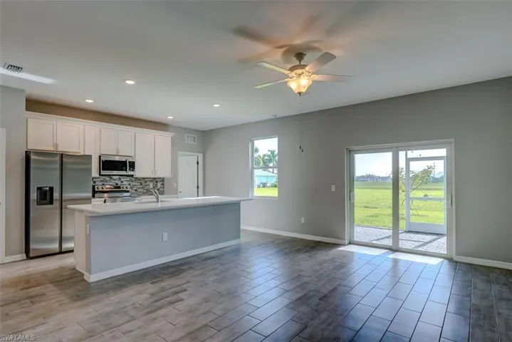Kitchen with a wealth of natural light, stainless steel appliances, a kitchen island with sink, and white cabinetry