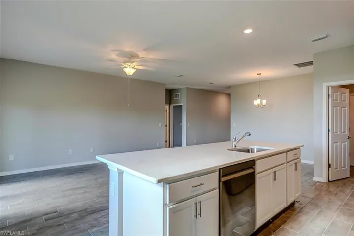 Kitchen with ceiling fan with notable chandelier, a center island with sink, dishwasher, sink, and white cabinets