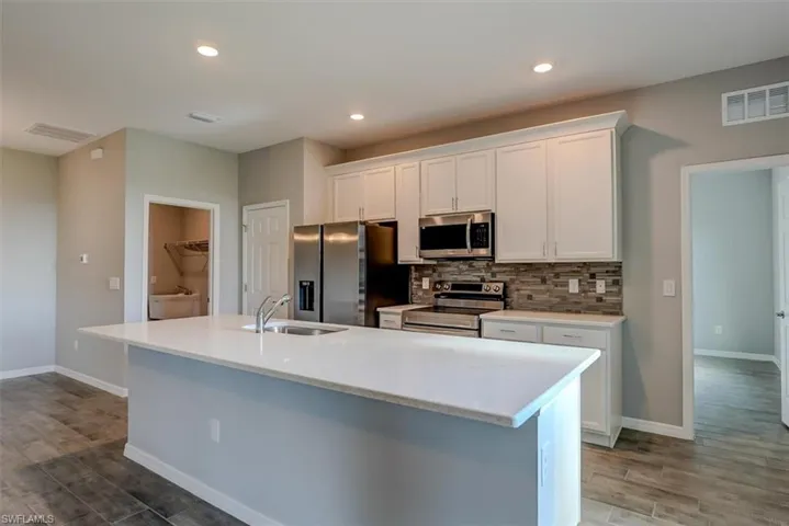 Kitchen with a kitchen island with sink, appliances with stainless steel finishes, sink, and white cabinets