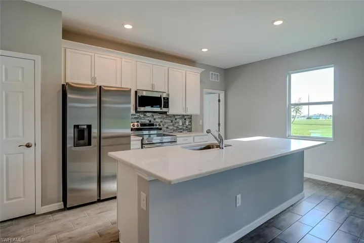 Kitchen with stainless steel appliances, white cabinetry, sink, an island with sink, and tasteful backsplash