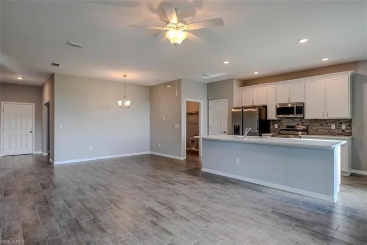 Kitchen with a kitchen island with sink, ceiling fan with notable chandelier, white cabinetry, decorative backsplash, and appliances with stainless steel finishes
